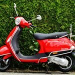 Bright red Vespa scooter parked against a lush green hedge, showcasing vibrant contrast.